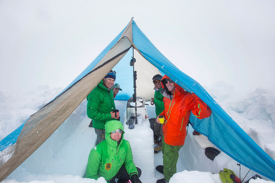 Five mountaineers are taking shelter in a tent on the lower Kahiltna glacier on Denali in Alaska. They are melting snow to cook food and have warm drinks.