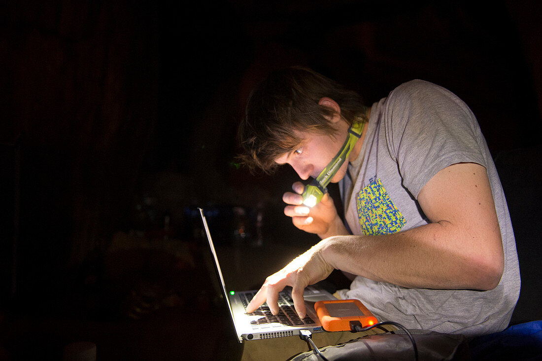 A man works on his laptop by the light of a headlamp