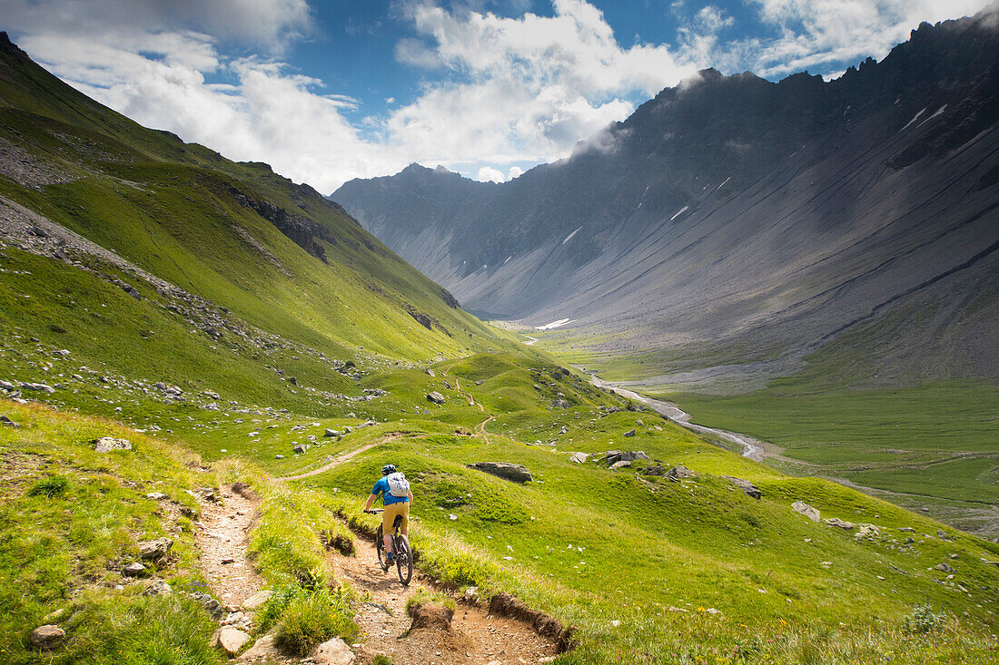 A Mountain Biker Riding Downhill In An Alpine Meadow Landscape