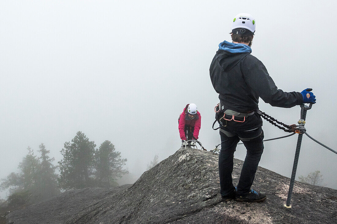 A man waits and looks back as a women climbs up the metal rungs of a Via Ferrata in Squamish, British Columbia.