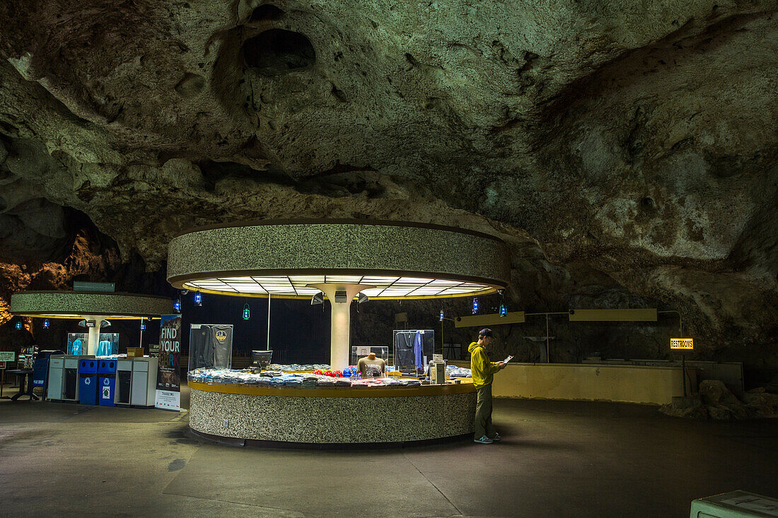 A man reads a map in the glow of a round information booth in a giant underground cavern.