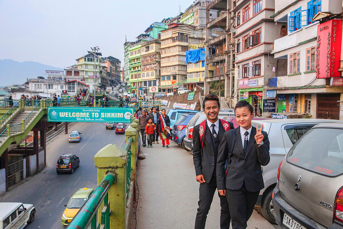 A young couple pose for the camera in front of a busy Sikkim street scene. Gangtok, Sikkim, India.