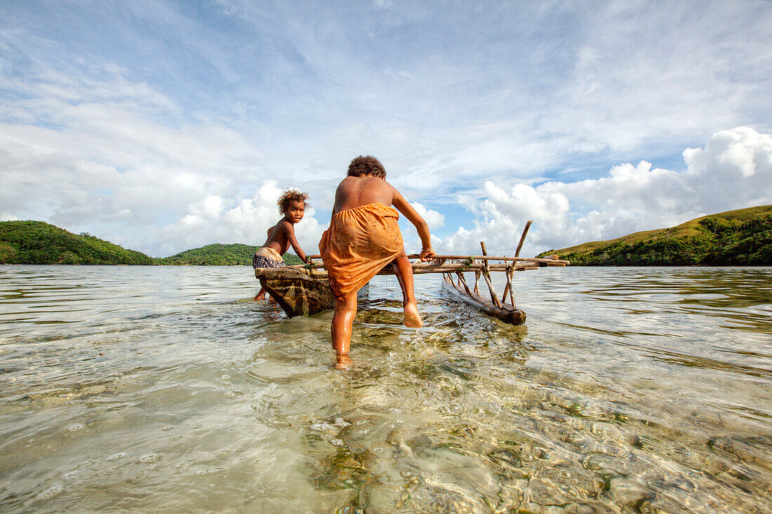 Children playing with a outrigger canoe in the village of Hessessai Bay at PanaTinai (Panatinane)island in the Louisiade Archipelago in Milne Bay Province, Papua New Guinea.  The island has an area of 78 km2. The Louisiade Archipelago is a string of ten l