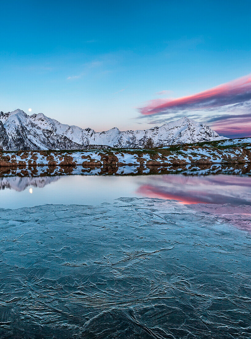 Tauwetter im alpinen See in der Dämmerung, der Mond Es spiegelt sich im See Gerola Tal, Valtellina, Lombardei, Italien, Europa