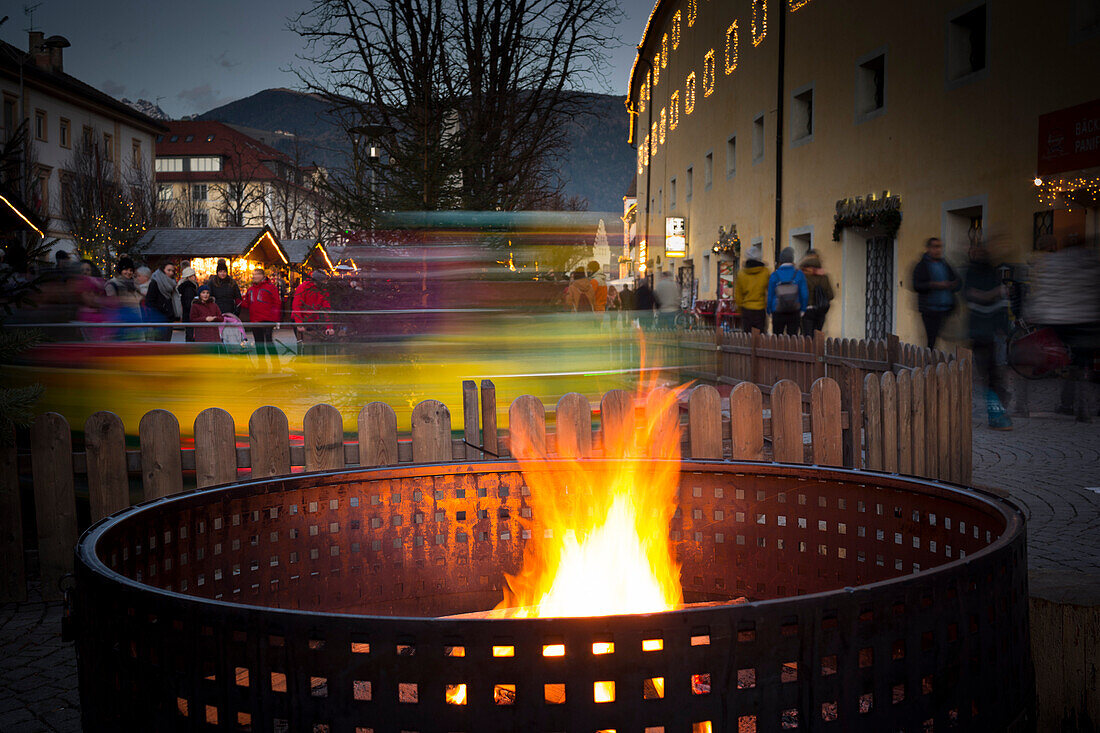 ein Bild von einem Lagerfeuer mit einem kleinen Zug hinter dem Feuer, während des Weihnachtsmarktes in der Stadt Bruneck, Provinz Bozen, Südtirol, Trentino-Südtirol, Italien, Europa