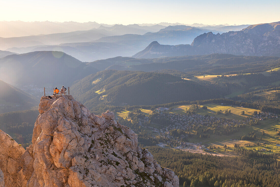 Hikers sitting on the top of Pulpito di Cima Popa - Poppekanzel at sunset looking to the horizon, Latemar, Bolzano, South Tyrol, Dolomites, Italy