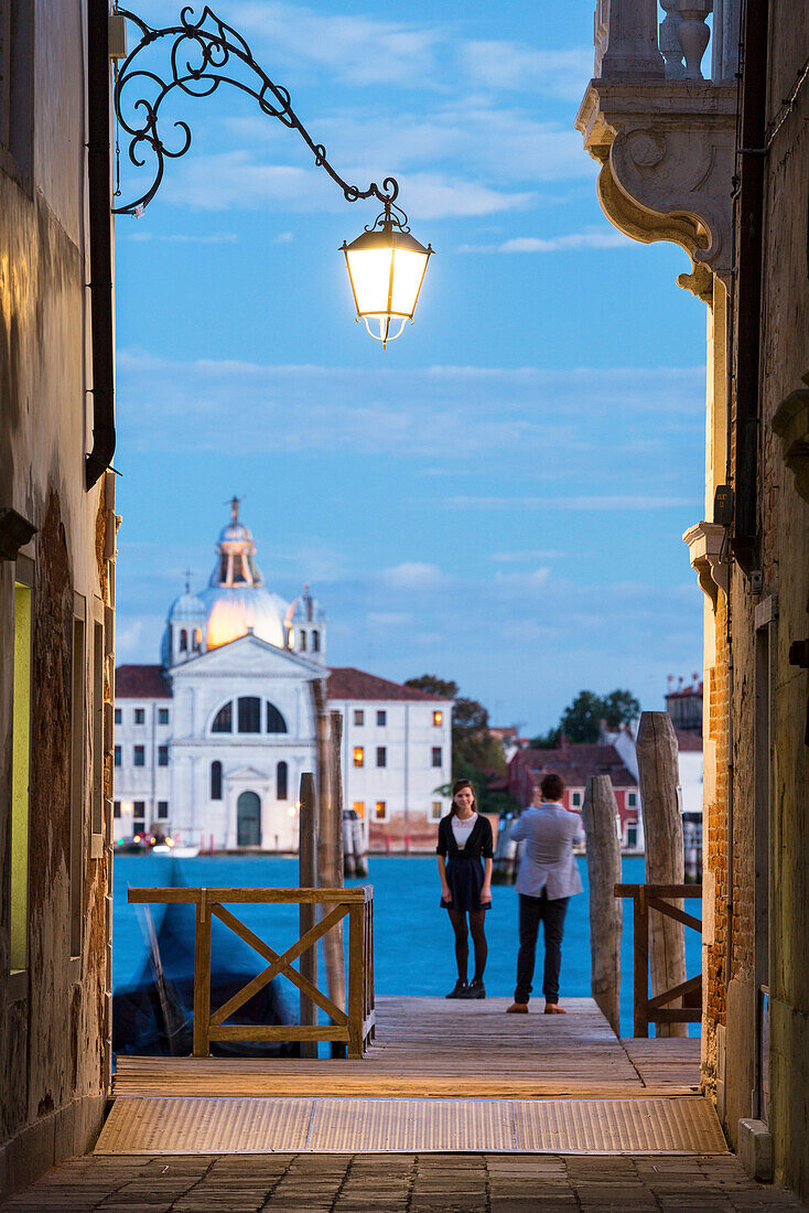 Tourists on the wood pier with the church Le Zitelle in the background framed by the lights of dusk Venice Veneto Italy Europe
