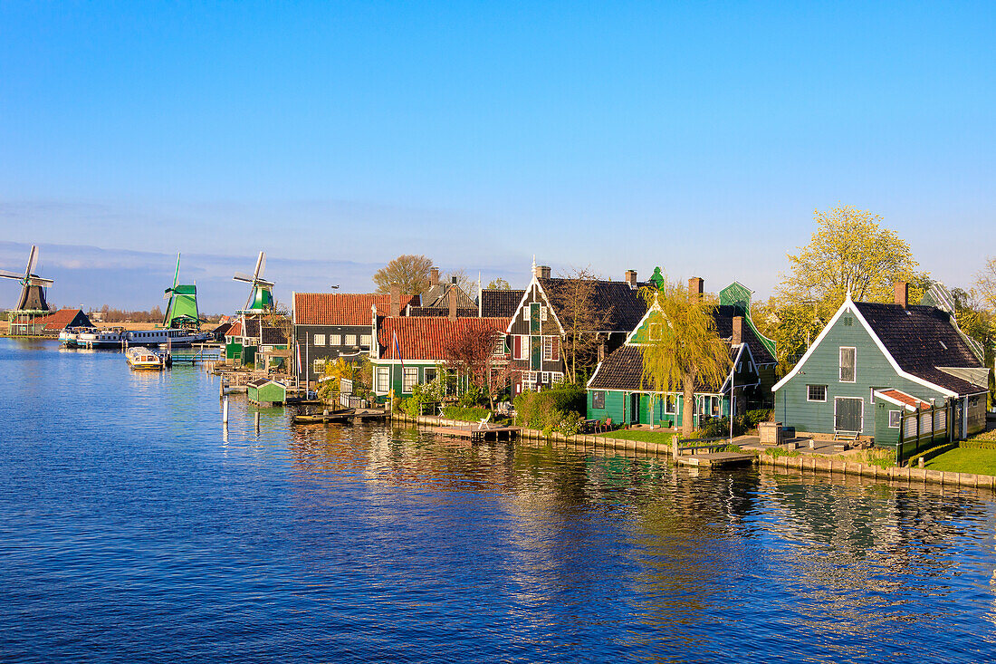 Wood houses and windmill are reflected in the blue water of river Zaan Zaanse Schans North Holland The Netherlands Europe