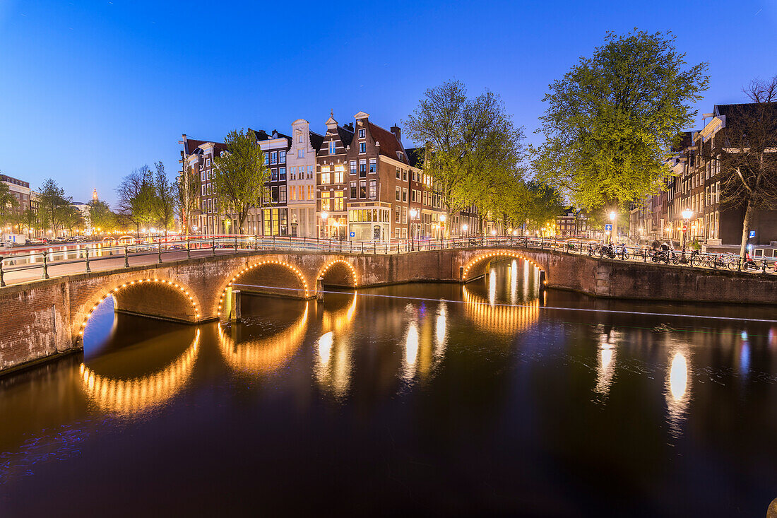 Dusk lights on the typical buildings and bridges reflected in a typical canal Amsterdam Holland The Netherlands Europe