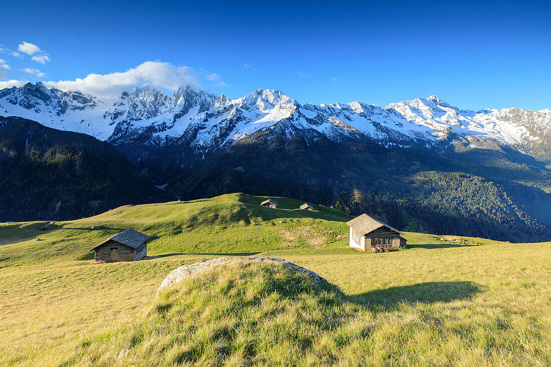Wiesen und Holzhütten im Frühjahr von schneebedeckten Gipfeln umrahmt Tombal Soglio Bregaglia Valley Kanton Graubünden Schweiz Europa
