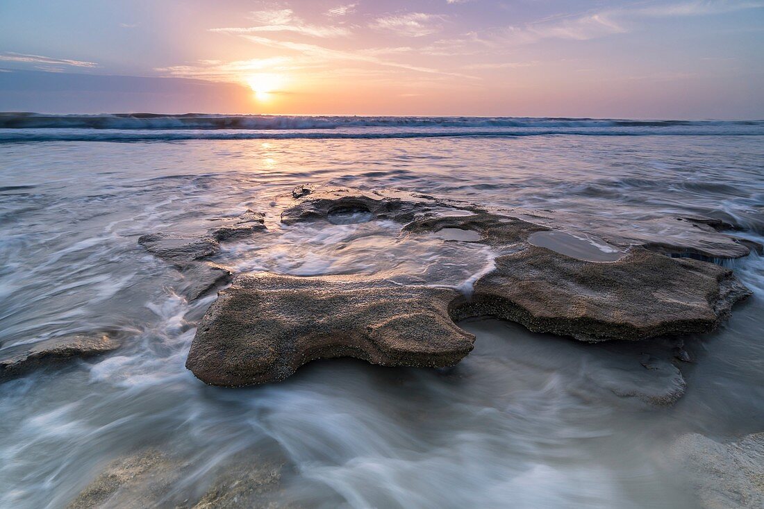 Sonnenaufgang über der ankommenden Gezeiten, die um einen Coquinafelsen bei Marineland Beach, Florida wirbeln.