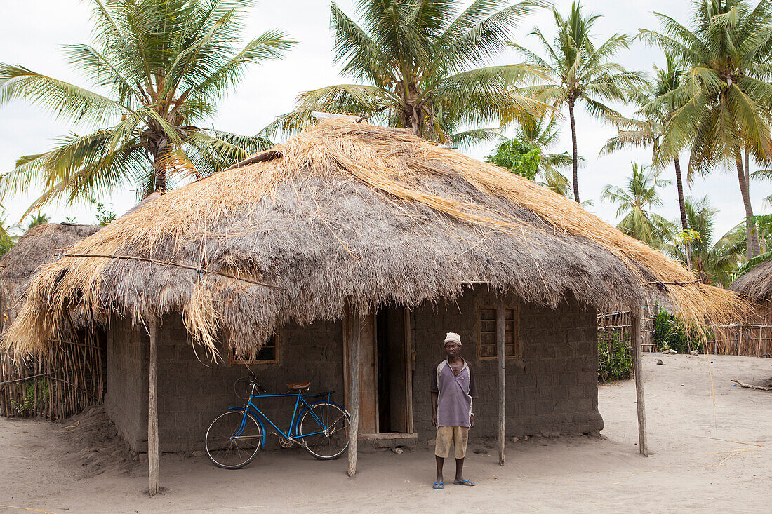 A man stands proudly outside his traditional mud hut home which has just been fitted with a solar panel, Tanzania, East Africa, Africa
