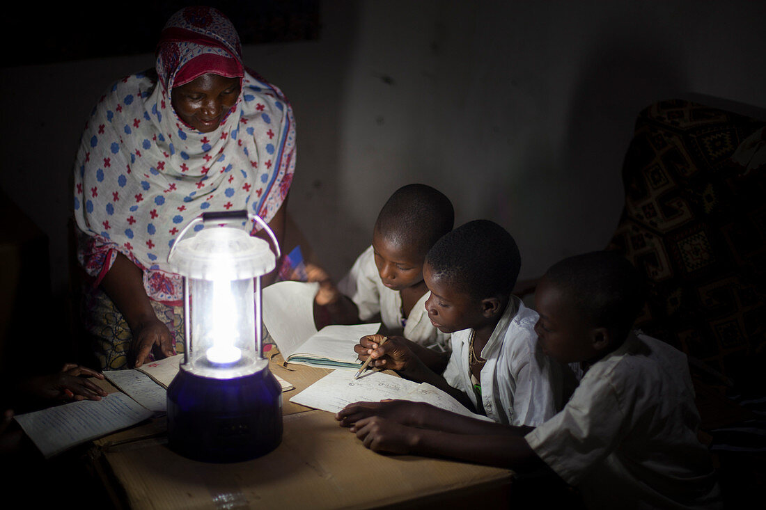 Eine Gruppe von Jungen liest ihre Hausaufgaben im Schein einer Sonnenlaterne, Tansania, Ostafrika, Afrika