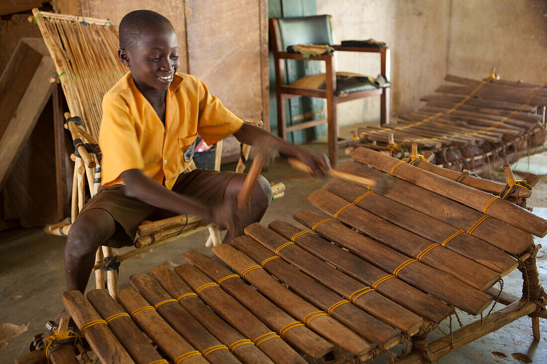 A school boy playing music on a large wooden xylophone at his primary school in Ghana, Africa