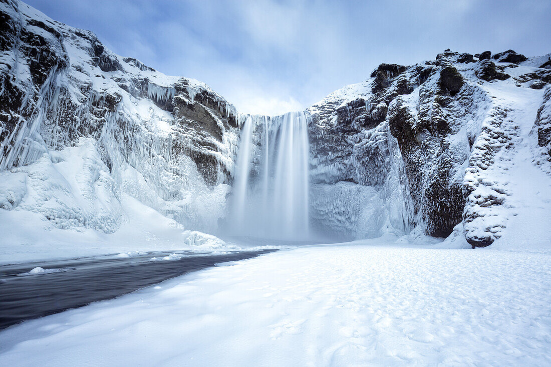 Winteransicht des Skogafoss-Wasserfalls, mit den Klippen bedeckt in den Eiszapfen und im foregreound bedeckt im Schnee, Skogar, Süd-Island, polare Regionen