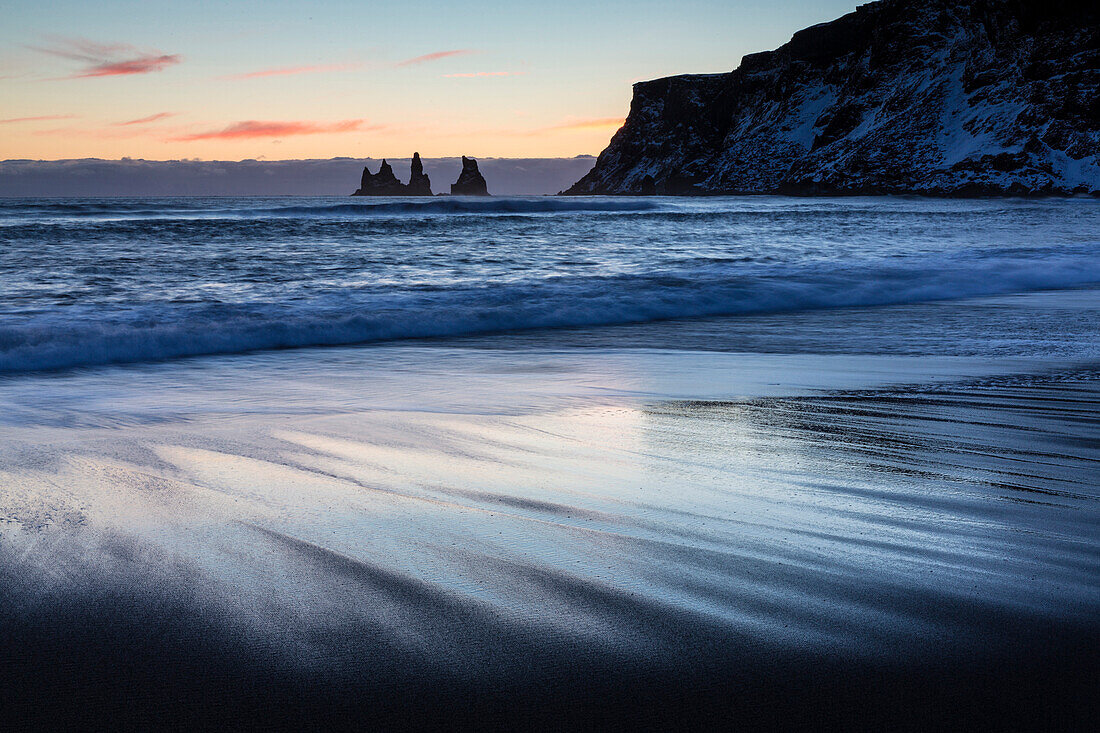 Wintersonnenuntergang auf dem schwarzen vulkanischen Sandstrand, der in Richtung zu den Felsstapeln von Reynisdrangar, Vik, Südisland, polare Regionen schaut