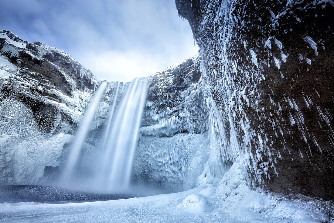 Winter view of Skogafoss waterfall, with cliffs covered in icicles and foregreound covered in snow, Skogar, South Iceland, Polar Regions