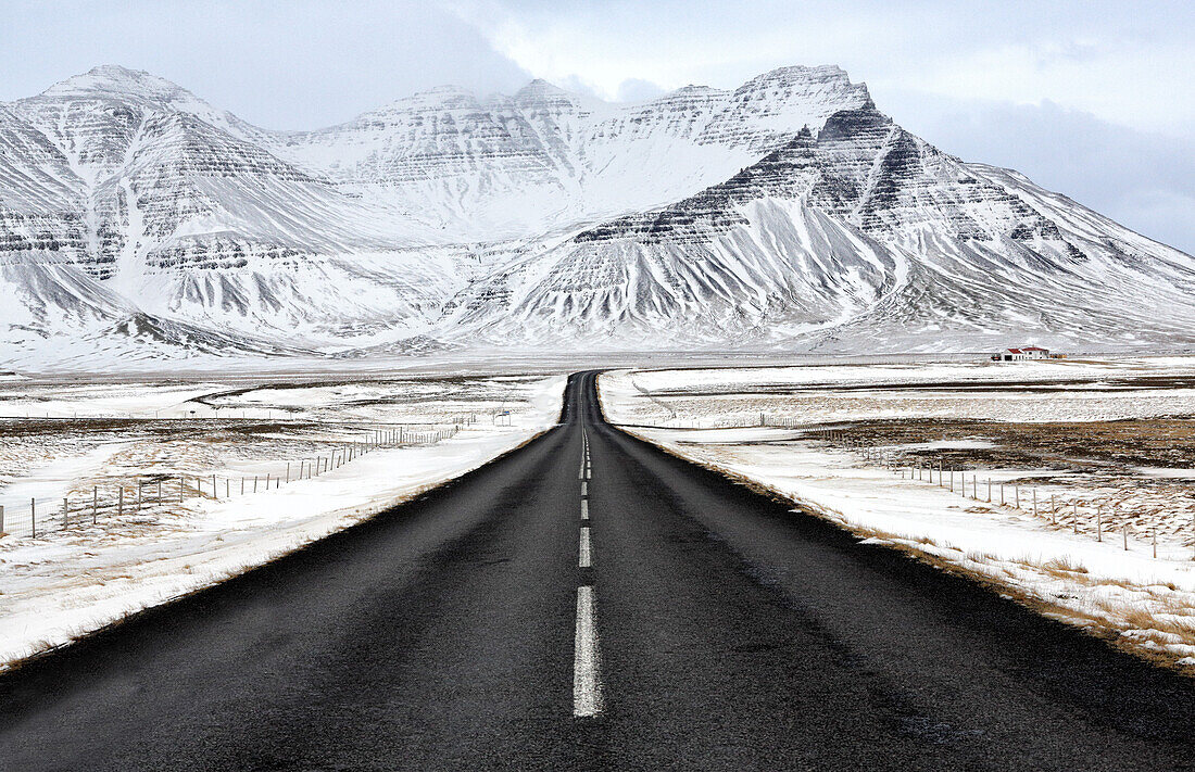 Die schwarze Asphaltstraße, die in Richtung zum Schnee führt, bedeckte Berge im Winter, Südisland, polare Regionen