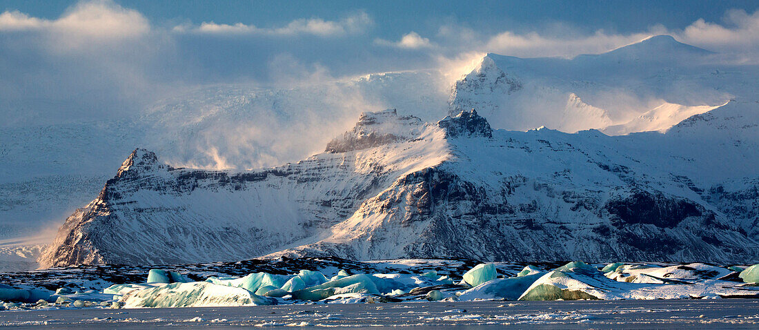 Winteransicht über gefrorene Jokulsarlon-Gletscher-Lagune, welche die blauen Eisberge zeigt, die im Schnee und in den entfernten Bergen, Südisland, polare Regionen bedeckt werden