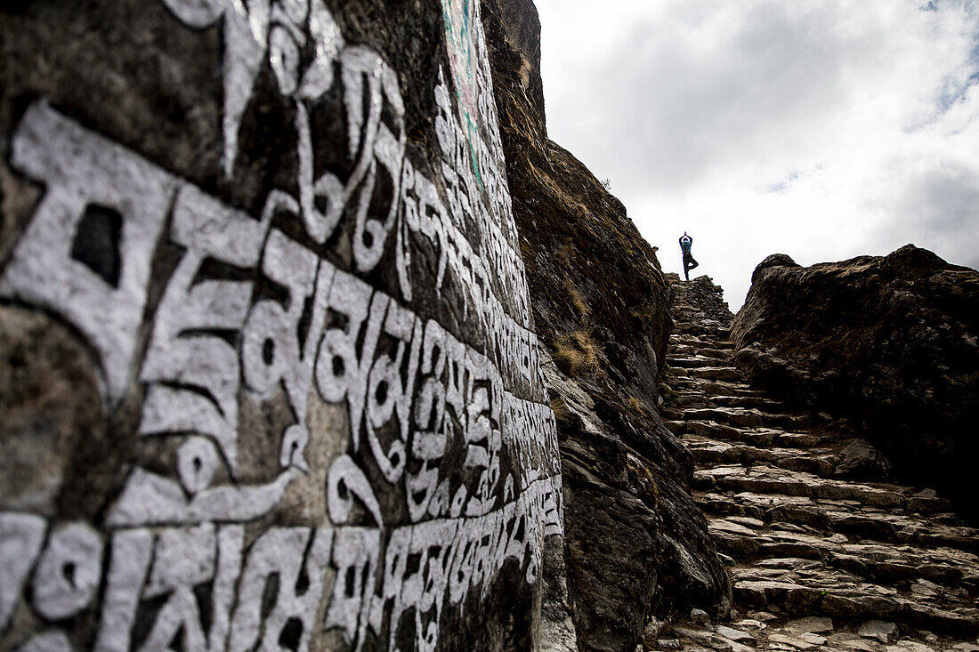Foto des Trekkers, der Yoga tut, werfen auf Everest-Basislager-Wanderung nahe der Wand auf, die mit tibetanischen Gebeten, Khumbu, Nepal geätzt wird