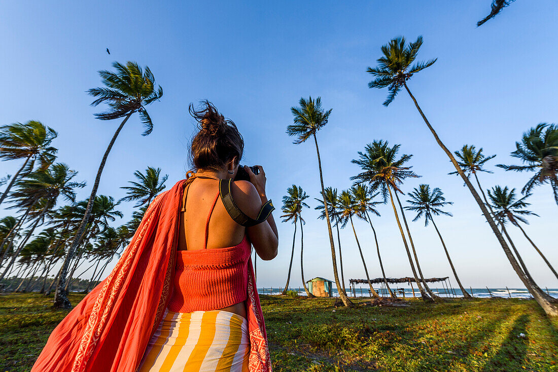 Rear view of female photographer in tropical scenery with coconut palm trees, Boipeba Island, south Bahia, Brazil