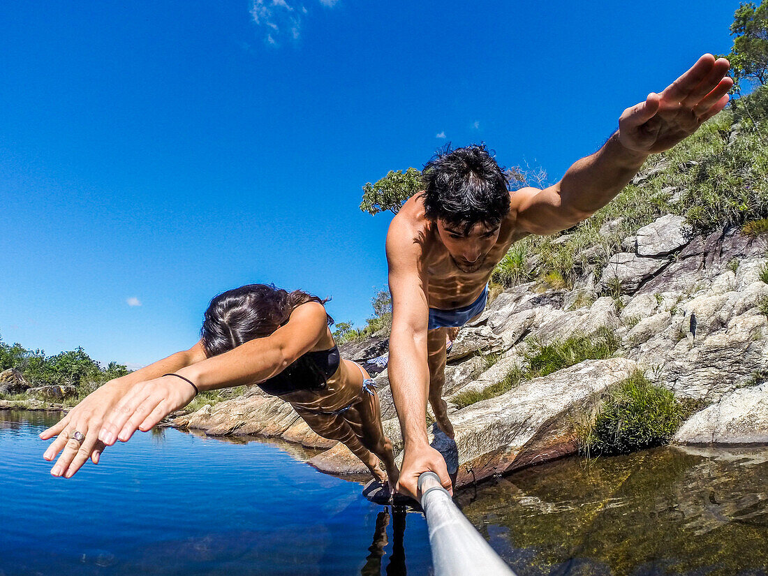 Photograph of couple taking selfie while jumping into river, Serra do Cipo National Park, Minas Gerais, Brazil
