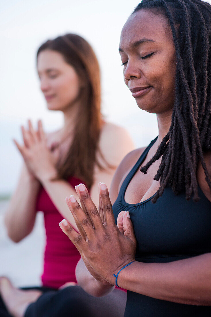 Photograph of two women meditating with eyes closed and hands clasped (Anjali mudra), Newport, Rhode Island, USA