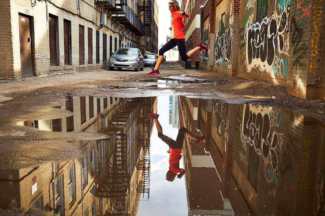 Woman running past puddle in graffiti lined alleyway in Boston, Massachusetts, USA