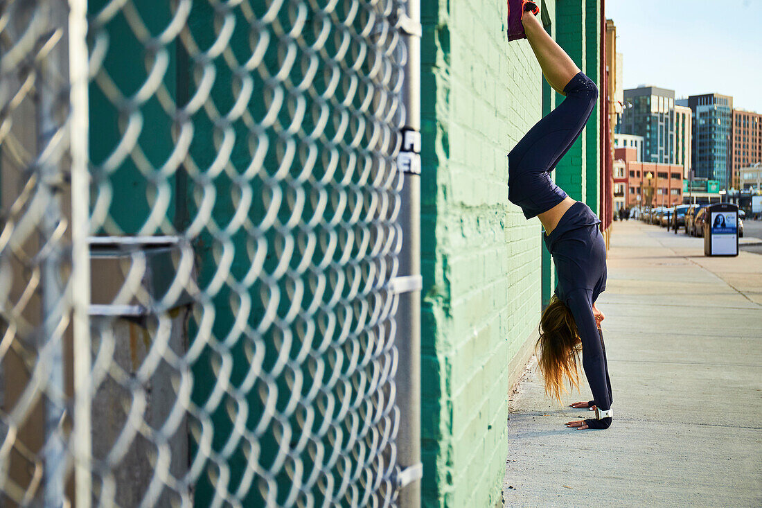Woman doing handstand on sidewalk beside chainlink fence, Boston, Massachusetts, USA