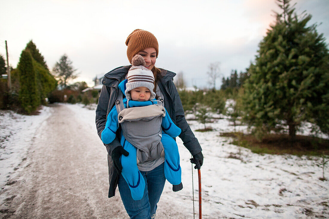 Mother walking with baby in carrier at Christmas tree farm, Langley, British Columbia, Canada