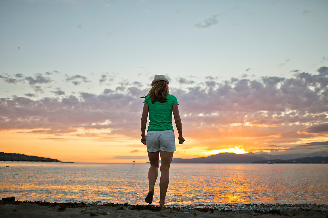 Rear view photograph of woman standing at Kitsilano Beach during sunset, Vancouver, British Columbia, Canada
