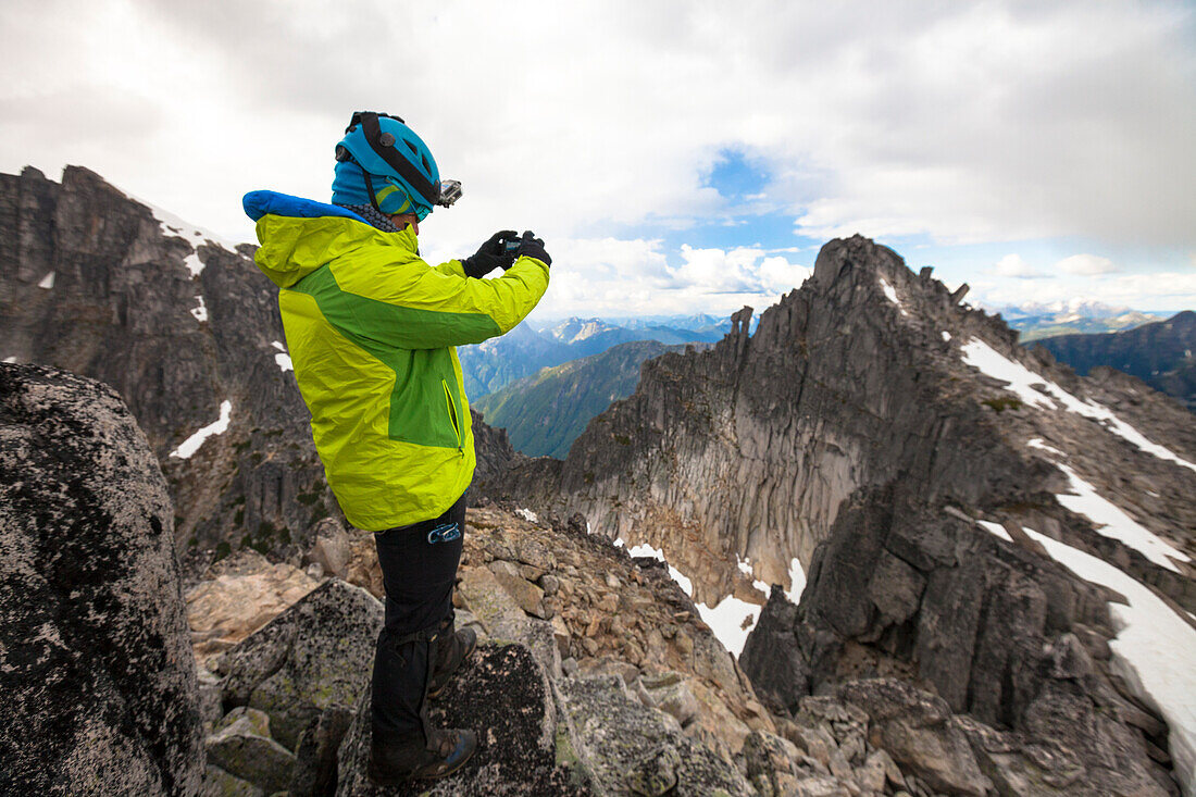 Side view photograph of mountaineer photographing mountain peak in North Cascade Mountain Range, Chilliwack, British Columbia, Canada