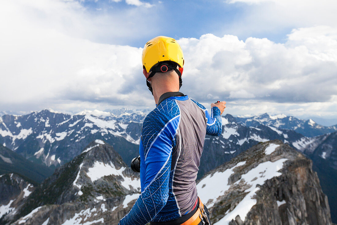 Photograph of mountain climber in safety helmet photographing view from summit of mountain in North Cascade Mountain Range, Chilliwack, British Columbia, Canada