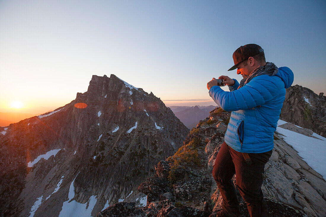 Mountaineer photographing view from mountain peak at sunset, Chilliwack, British Columbia, Canada