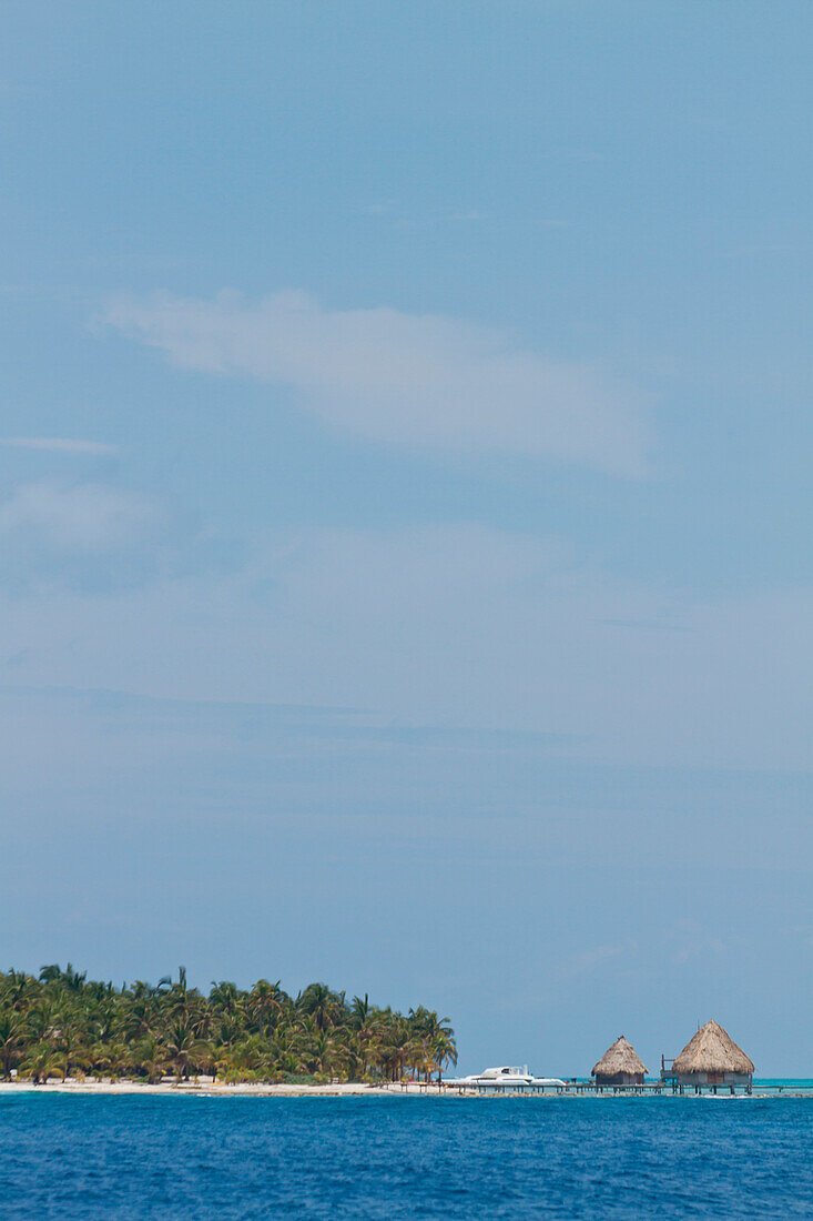 Strohdachhütten sitzen über dem Ozean vor einer Insel in der Gegend von Glover's Reef, Belize.