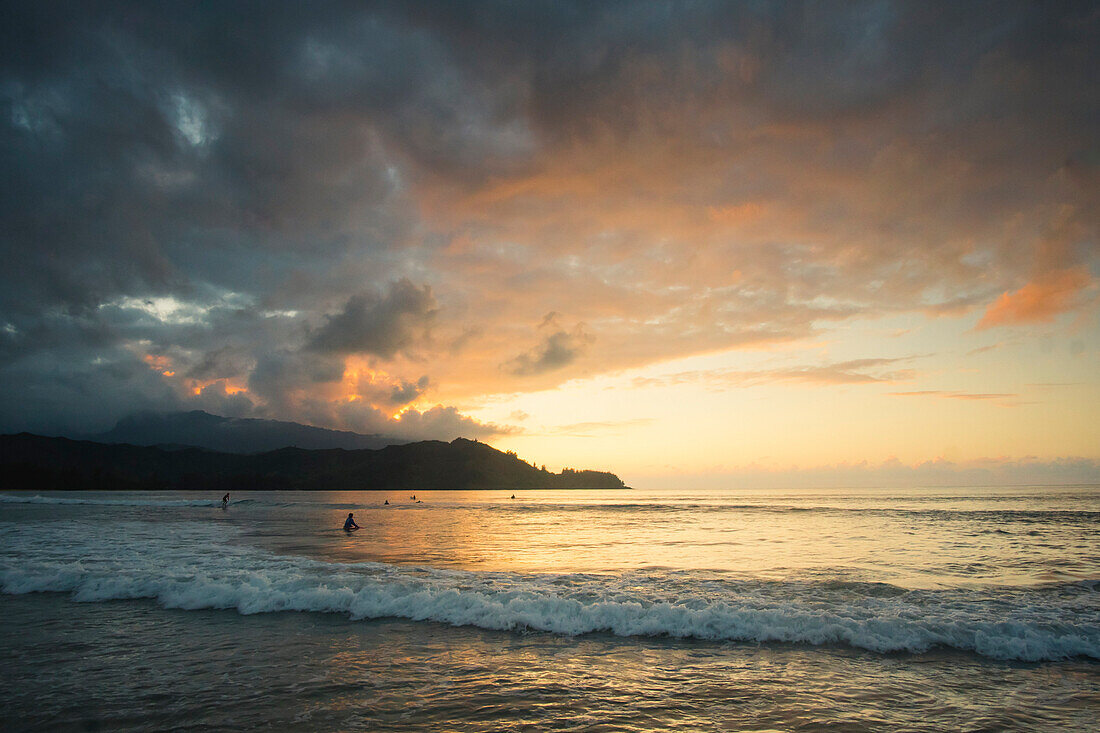 Surfer warten, bis die Sonne hinter den Bergen in Hanalei Bay, Kauai, Hawaii untergeht