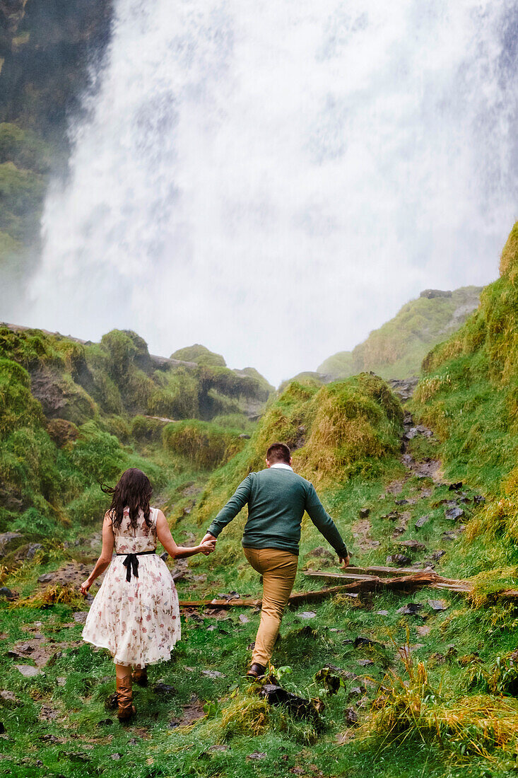 Rear view photograph of couple walking while holding hands at Sahalie Falls on McKenzie River, Oregon, USA