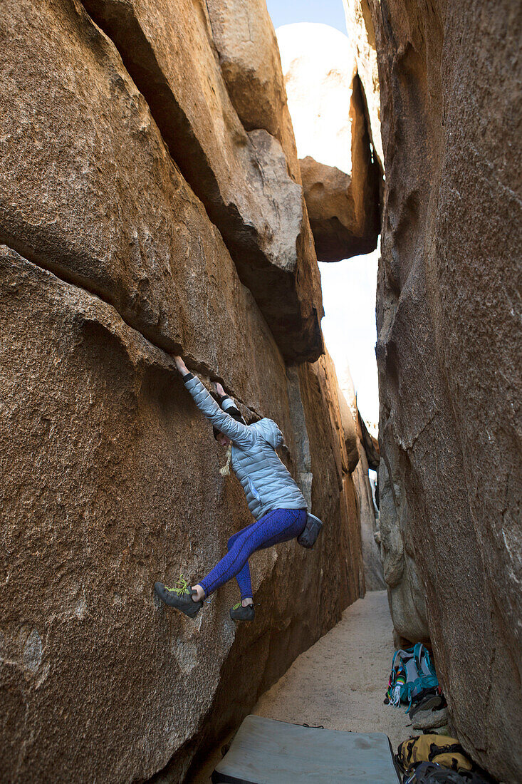 Woman climbing rock wall of crevasse in Joshua Tree National Park, California, USA