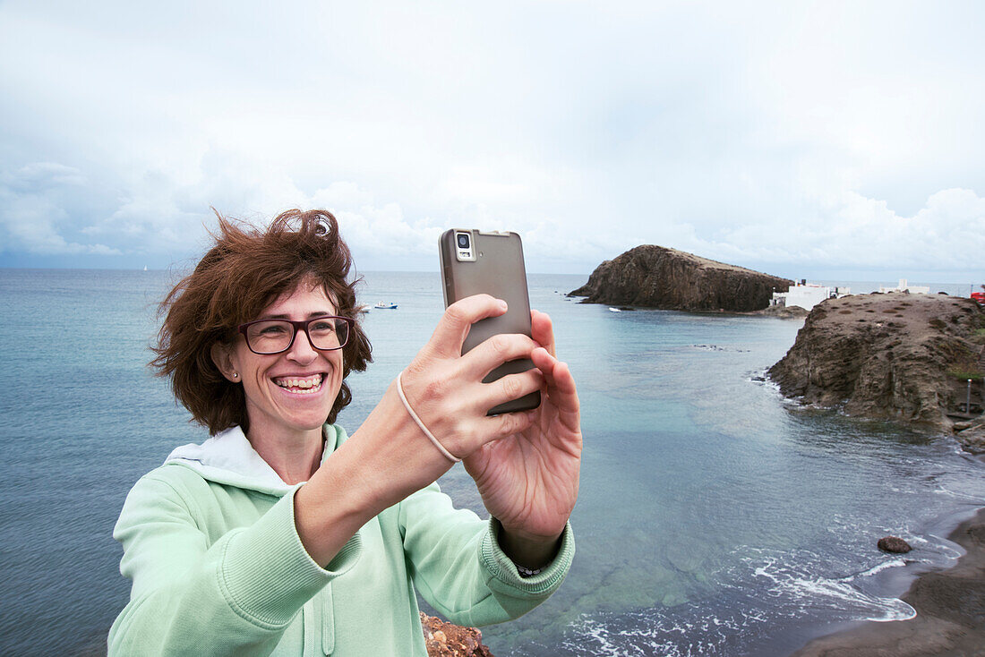 Lächelnde Frau beim Nehmen von selfie vor Meer, Almeria, Andalusien, Spanien