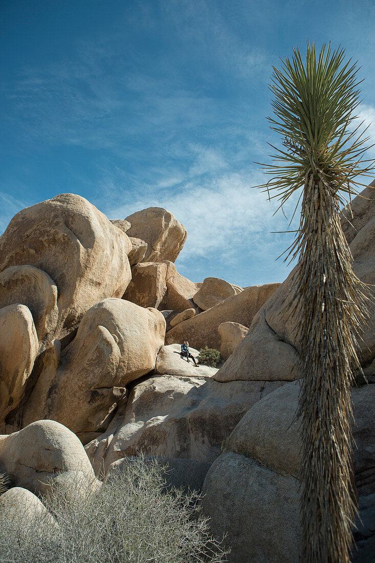 Photograph of woman sitting on large rock formation in Joshua Tree National Park, California, USA