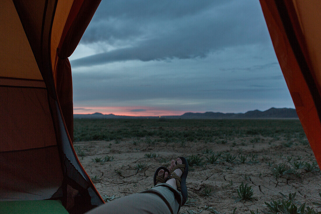 Photograph of feet of person sticking out of tent at sunset in dried up lake basin in Joshua Tree National Park, California, USA