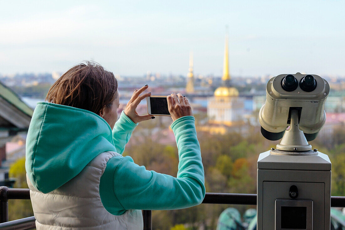 Junge Frau mit Telefon an der Aussichtsplattform von St. Isaacs Cathedral, Admiralität und Peter und Paul Cathedral im Hintergrund, St Petersburg, Russland