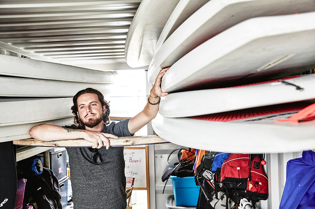 Der junge bärtige Mann, der paddleboard vom Behälter zieht, füllte mit Schwimmenausrüstung, Portland, Maine, USA.