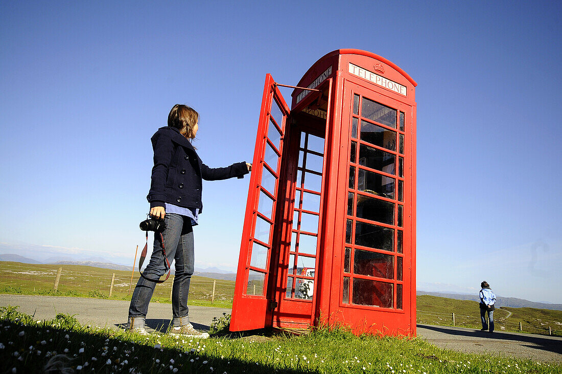 Mädchen sieht in Telefonzelle bei Elgol, Isle of Skye, Schottland