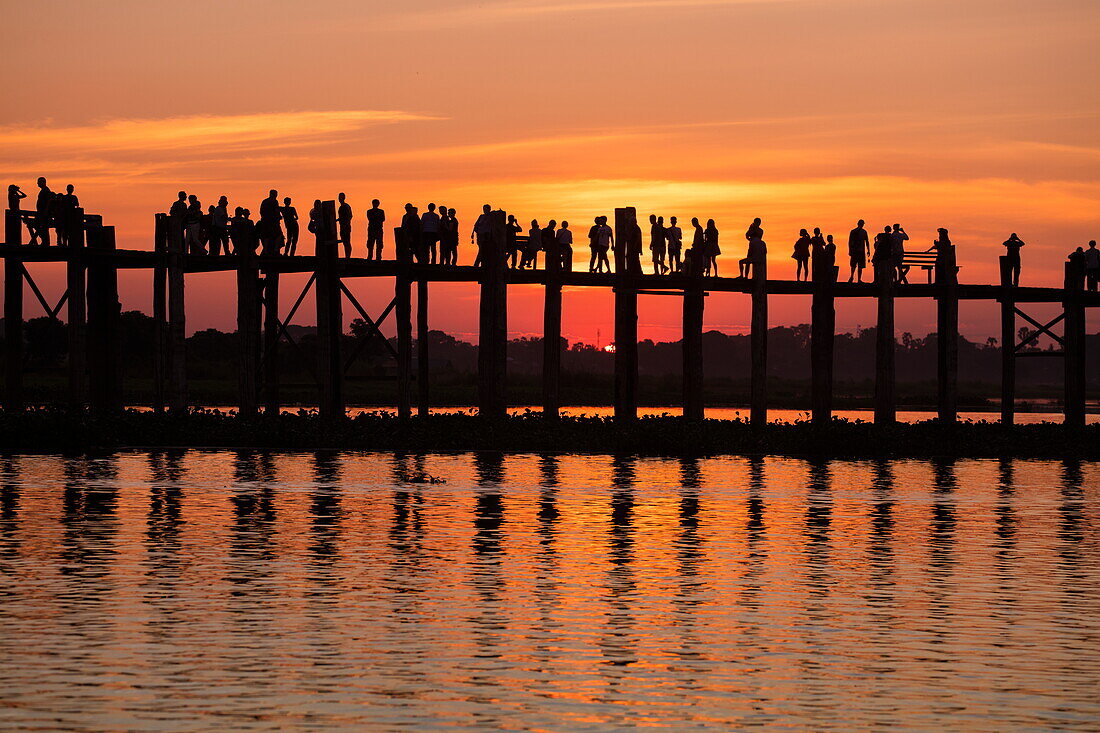 Silhouette of people walking along U Bein Bridge across Taungthaman Lake at sunset, Amarapura, Mandalay, Myanmar