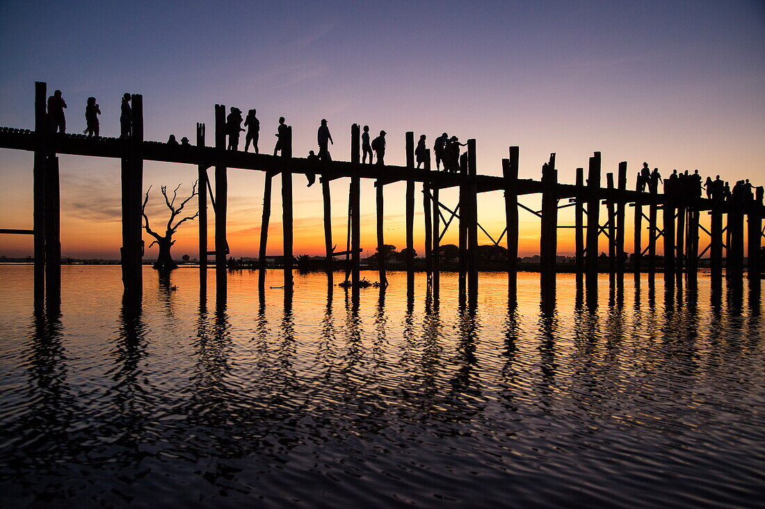 Silhouette of people walking along U Bein Bridge across Taungthaman Lake at sunset, Amarapura, Mandalay, Myanmar