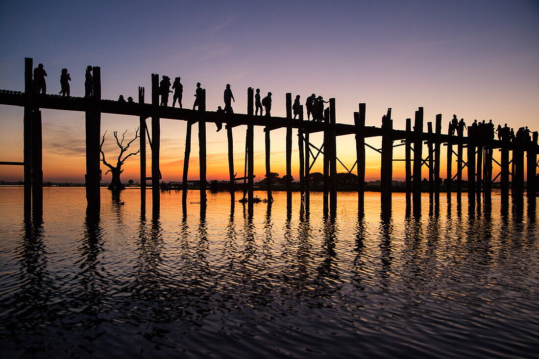 Silhouette von Menschen die auf der U-Bein-Brücke über den Taungthaman See laufen bei Sonnenuntergang, Amarapura, Mandalay, Myanmar