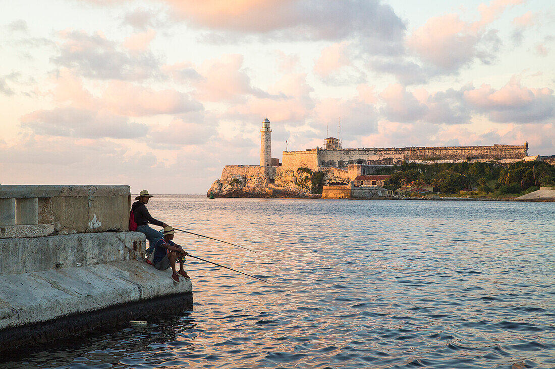 Kubanische Fischer auf dem Malecon-Damm mit dem Castillo De Los Tres Reyes Del Morro im Hintergrund