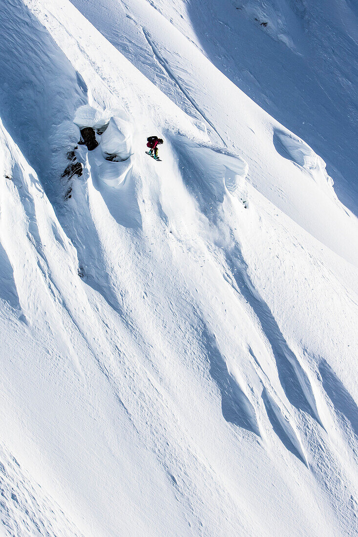 Professional snowboarder Helen Schettini, catches air and grabs her board on a sunny day while snowboarding in Haines, Alaska.