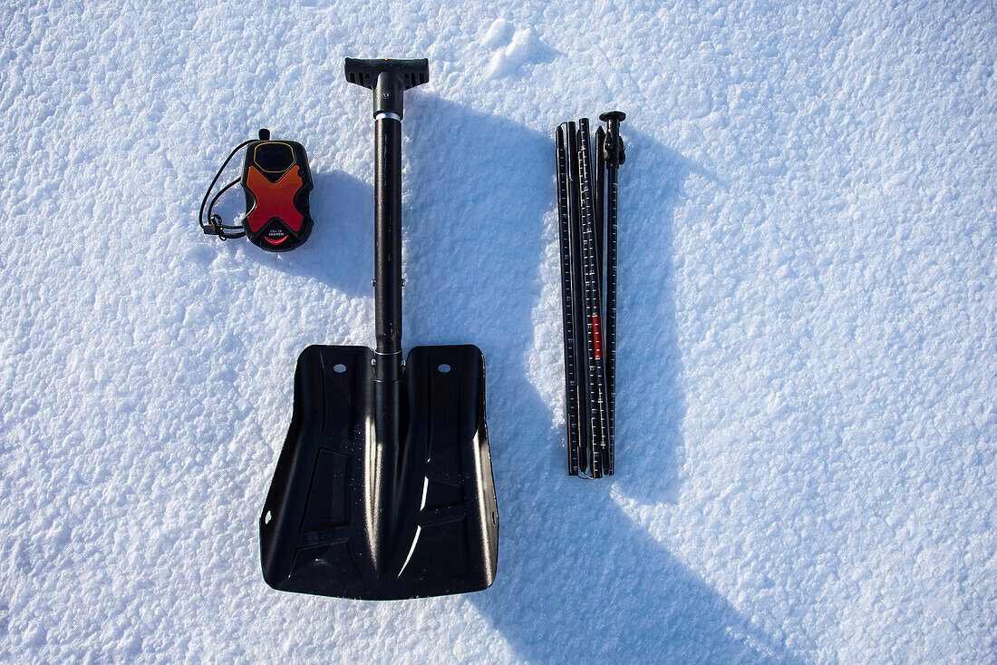 Ein Leuchtfeuer, Schaufel und Sonde, das Wesentliche zu einem Backcountry-Enthusiasten-Kit werden auf dem Schnee angezeigt.